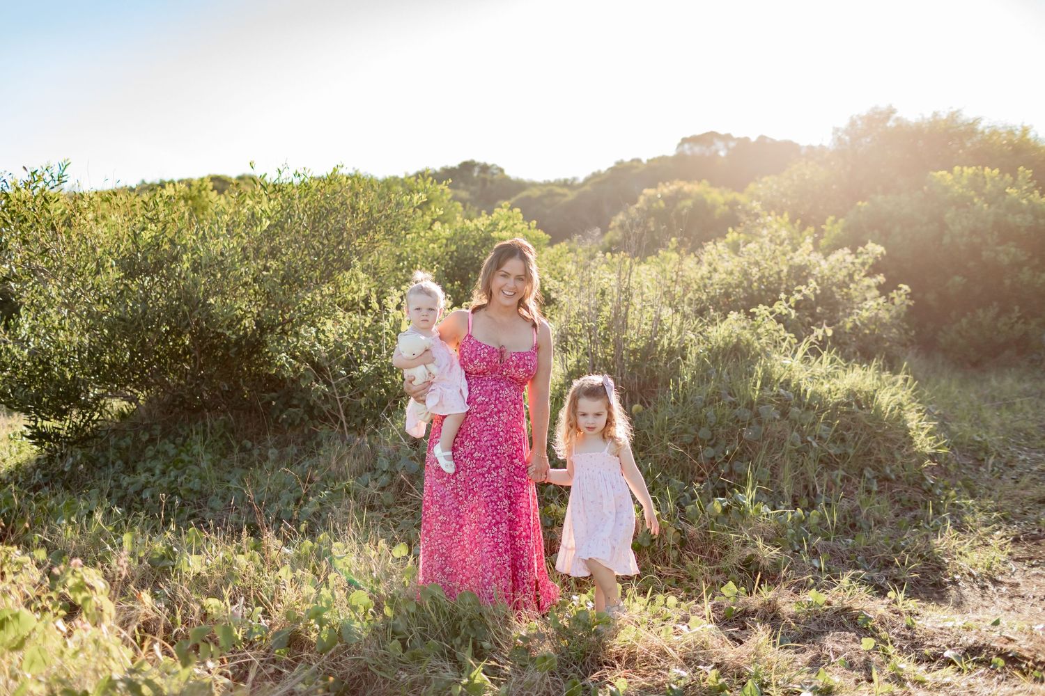 A family portrait taken in natural sunlight among green foliage.