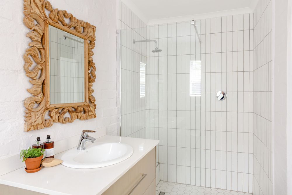 Modern white bathroom with ornate gold mirror and glass shower enclosure.