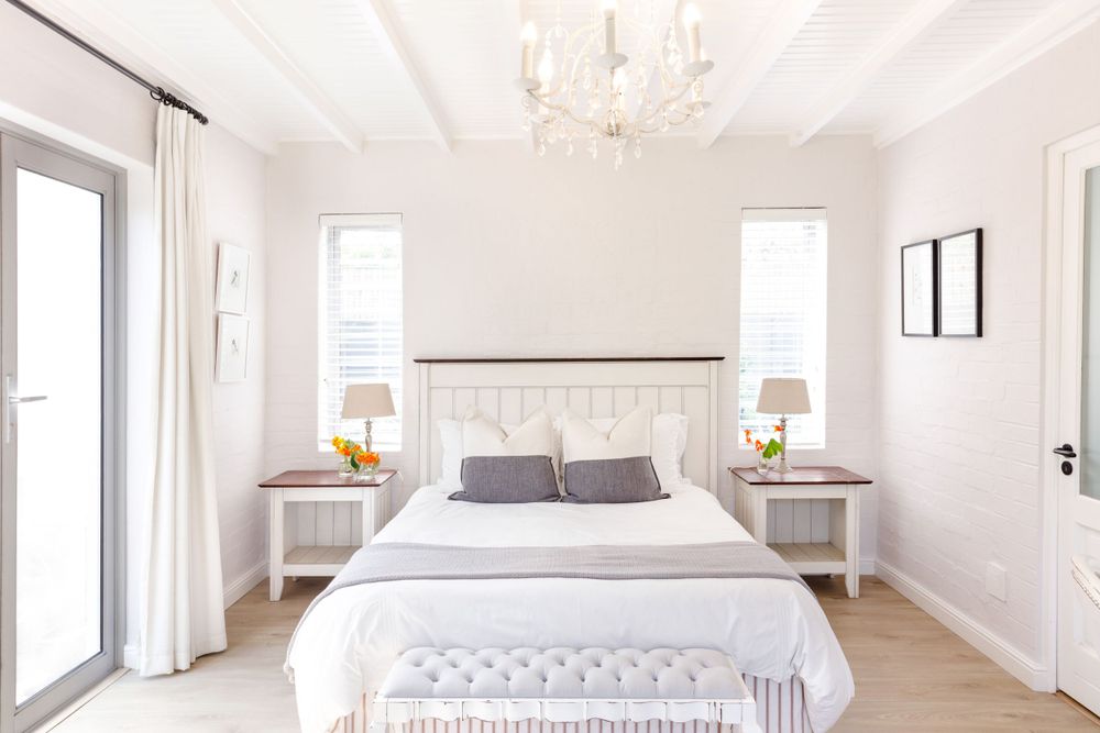 Bright white bedroom with chandelier, twin nightstands, and crisp bedding.