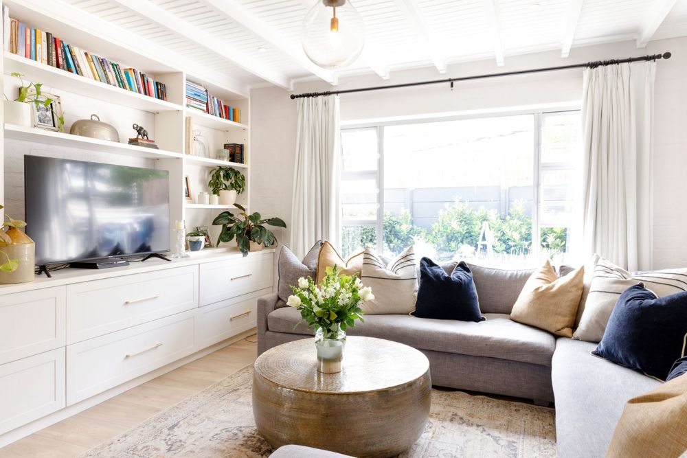 Bright living room with built-in white shelving unit, gray sectional sofa, and round coffee table near large windows.