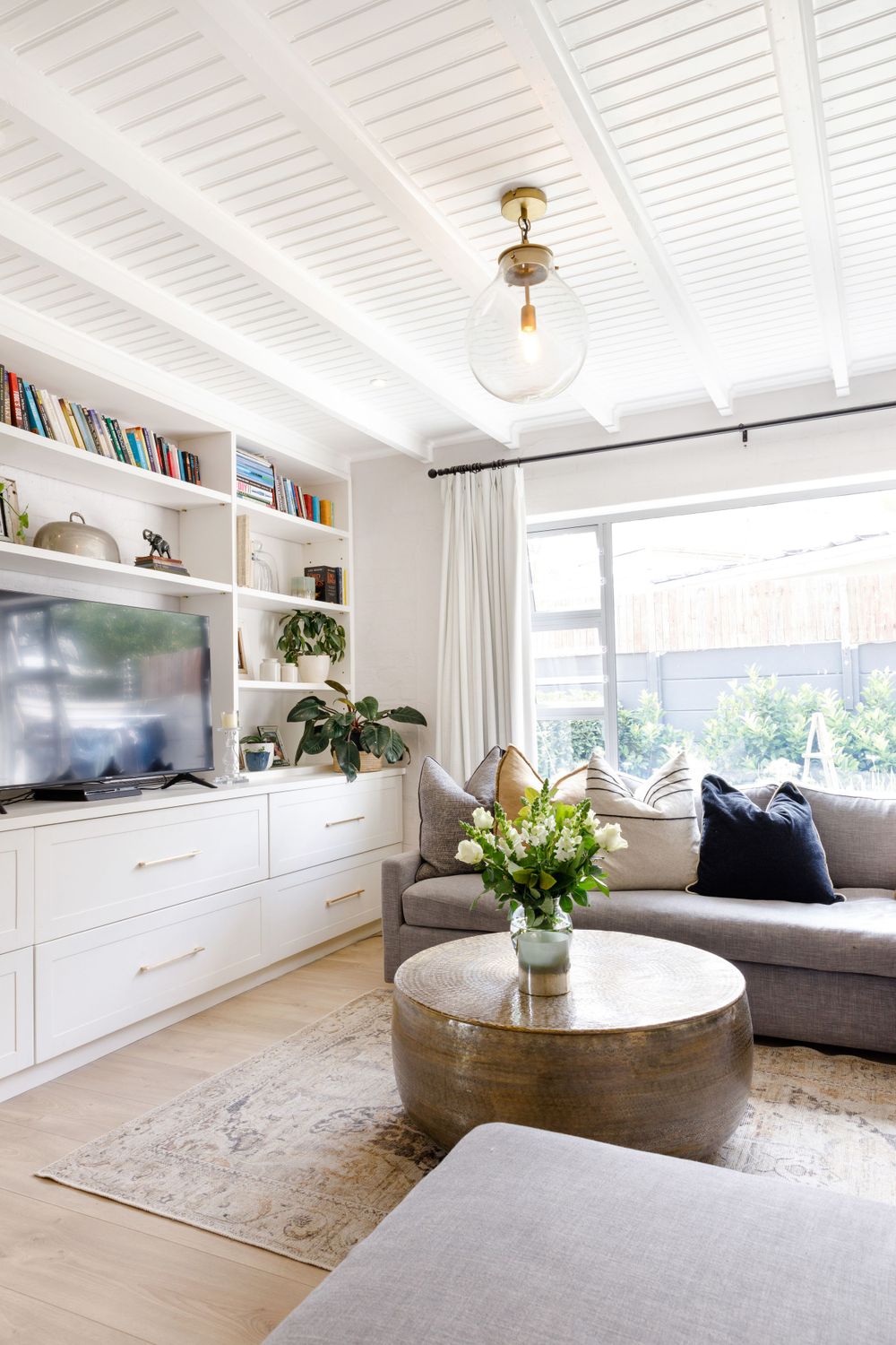 Modern white living room featuring wall-mounted TV, built-in shelves, and gray sectional with navy pillows.