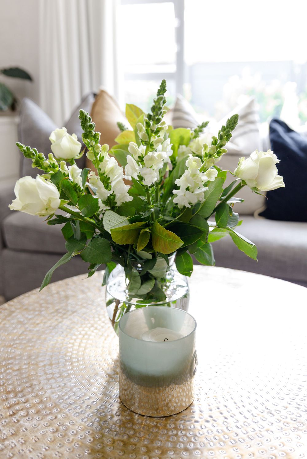 White and green floral arrangement with roses in glass vase on round table.