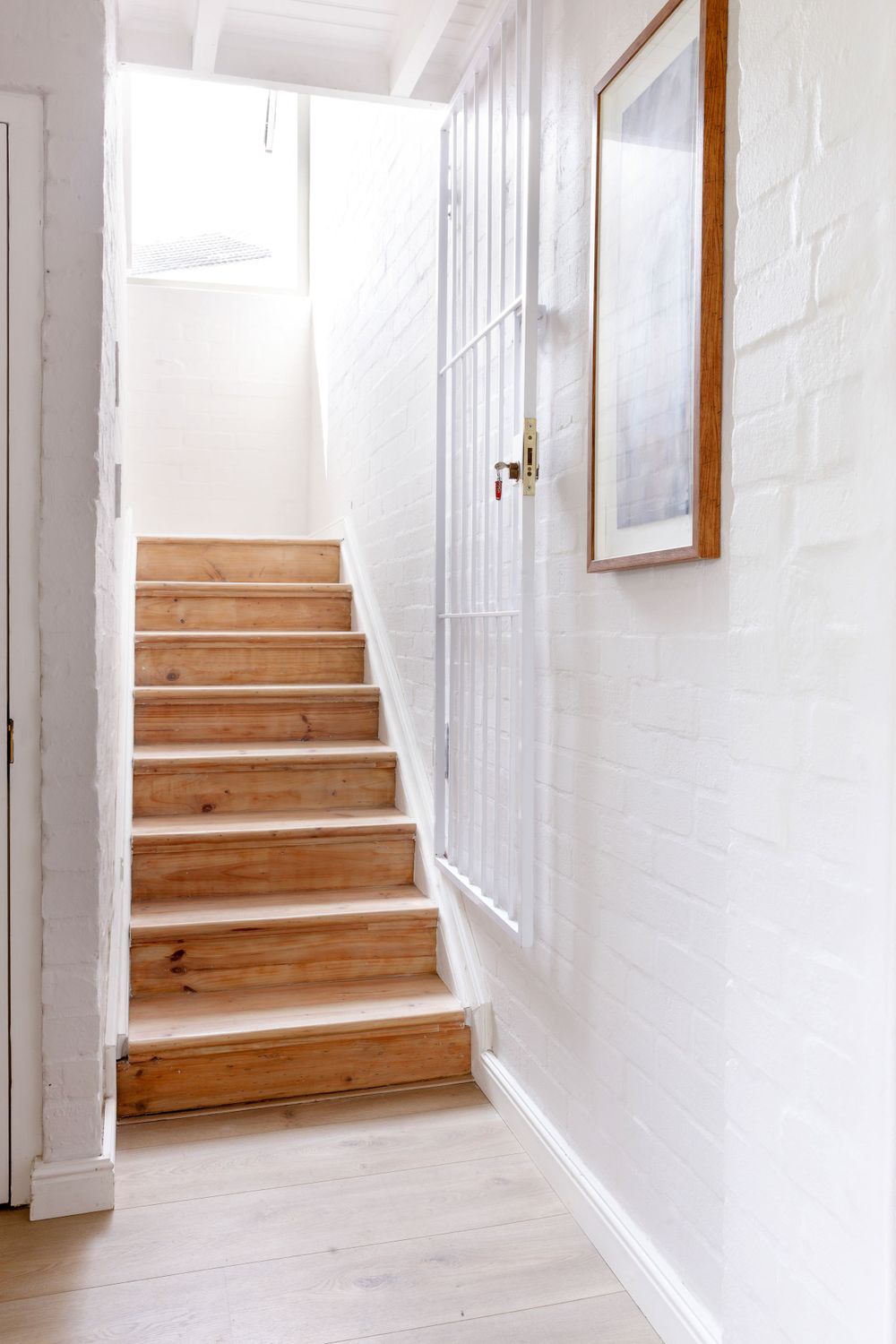 White painted staircase with natural wood steps and a framed mirror on the wall.