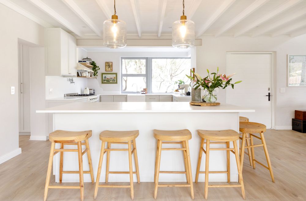 Modern white kitchen with light wood bar stools and pendant lighting over large island.