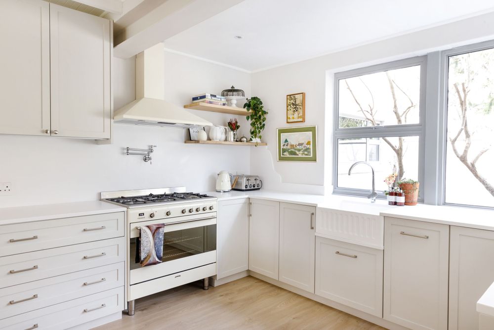 Clean white kitchen with stainless steel range, white cabinets, and large windows.