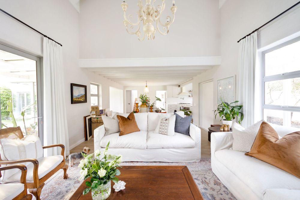 Bright coastal living room with white sofas, tan pillows, and floral arrangements.