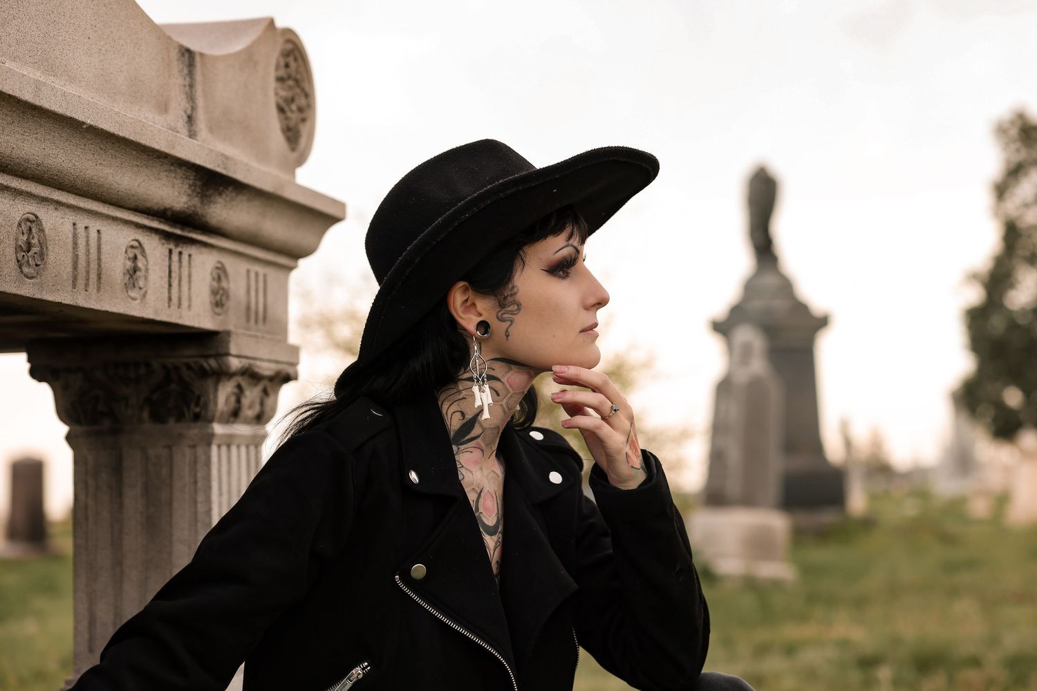 Gothic style photo of person in black hat and leather jacket at cemetery.