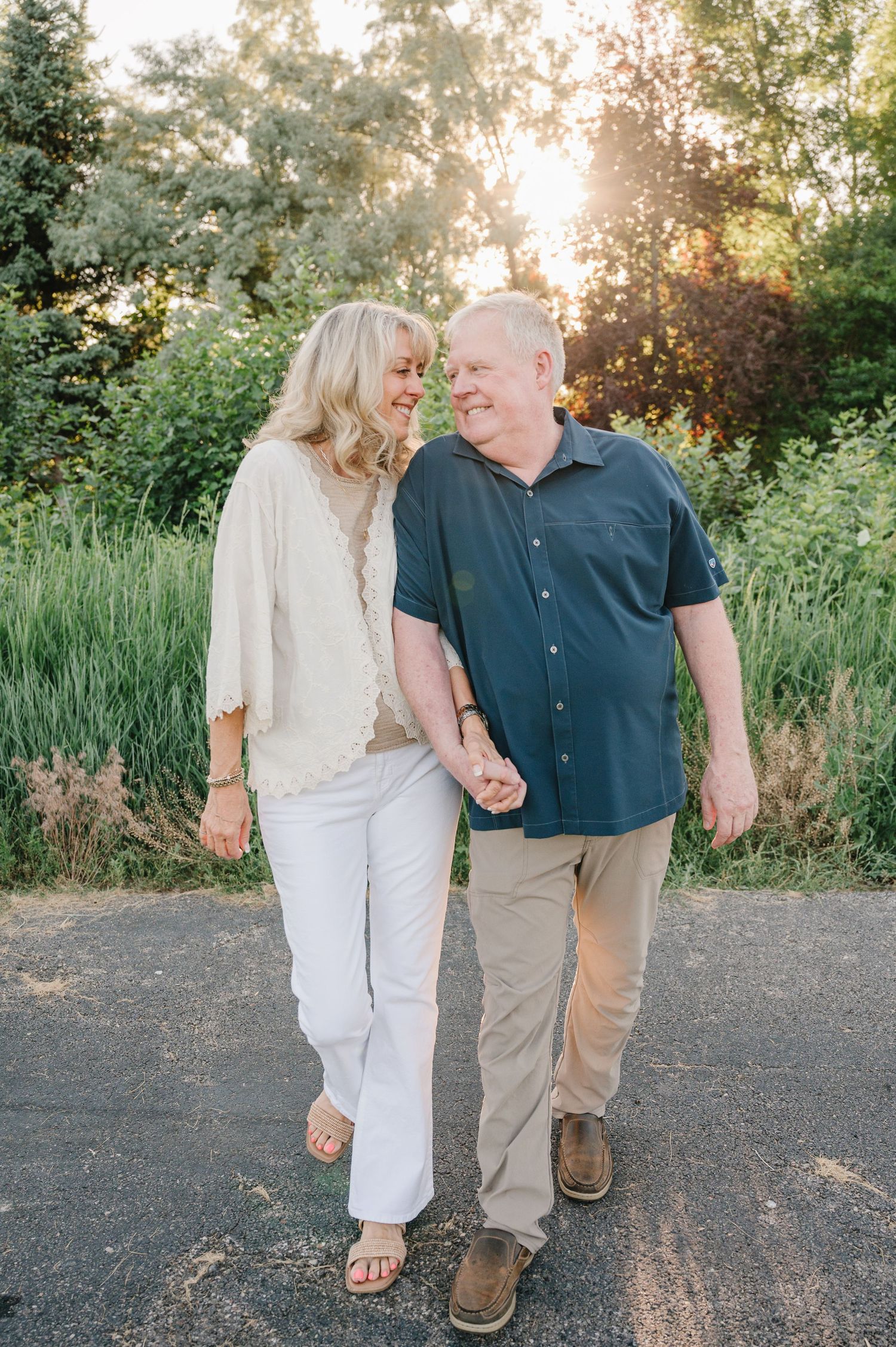 Couple walking together on a path during golden hour sunset with lush greenery in background.