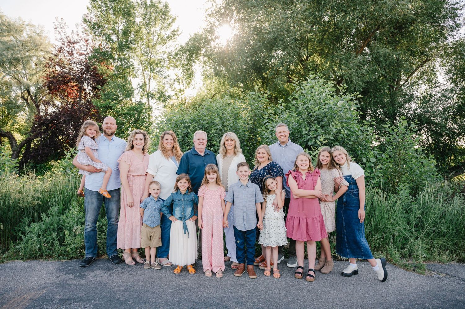 Large family group posing for outdoor portrait with coordinated outfits against natural greenery.