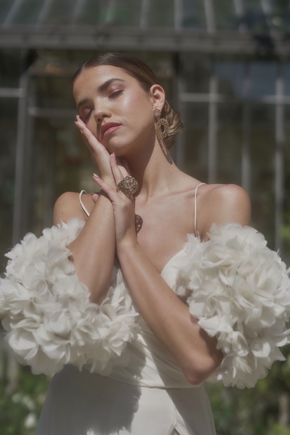 Fashion portrait with dramatic ruffled white sleeves and elegant bridal jewelry in dreamy sunlit setting.