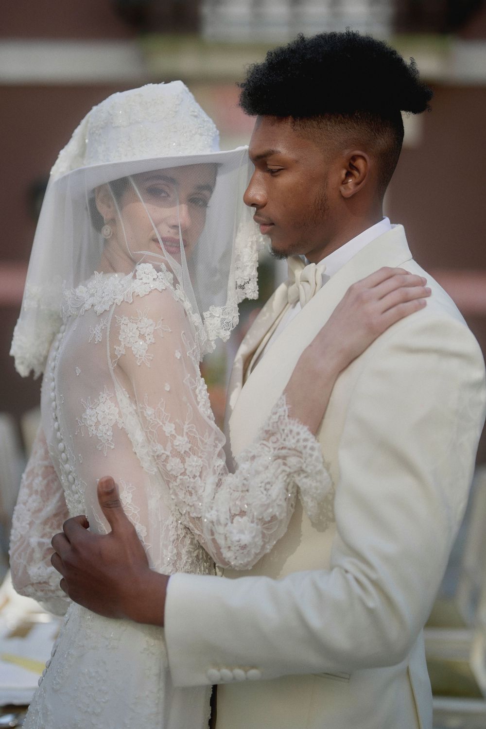 A bride and groom share an intimate moment in their wedding attire, with her wearing a delicate lace veil.