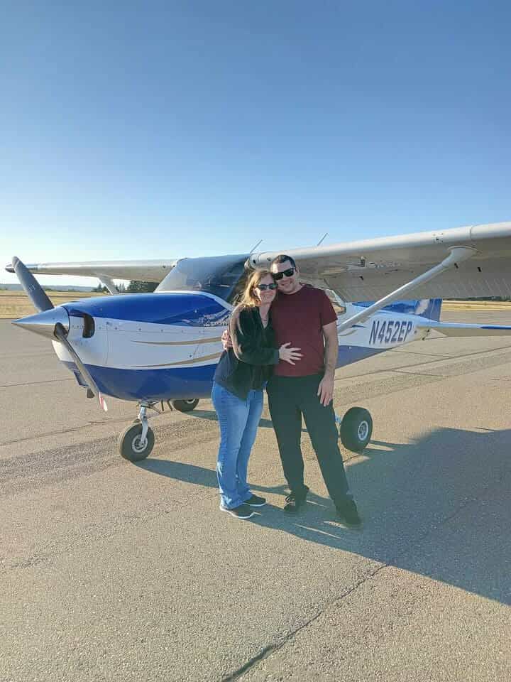 A couple poses in front of a small blue and white private aircraft on an airport tarmac.