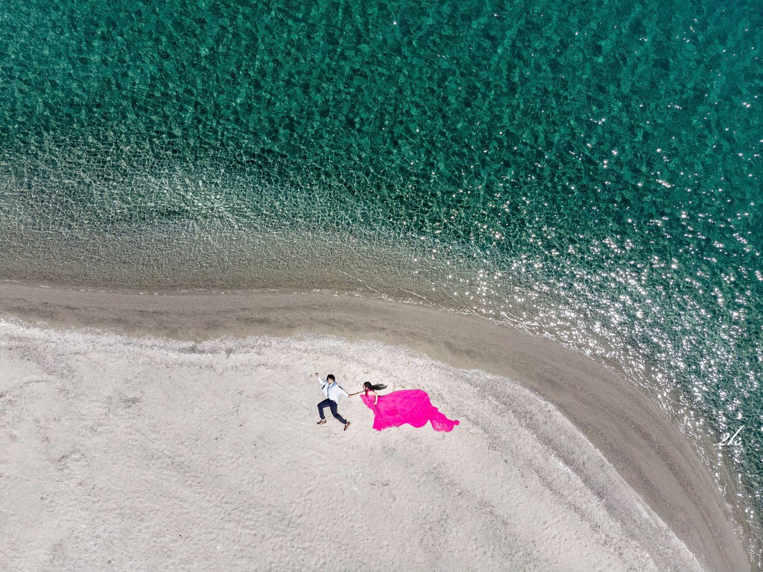 Aerial view of a beach scene with turquoise water and pink fabric on white sand.