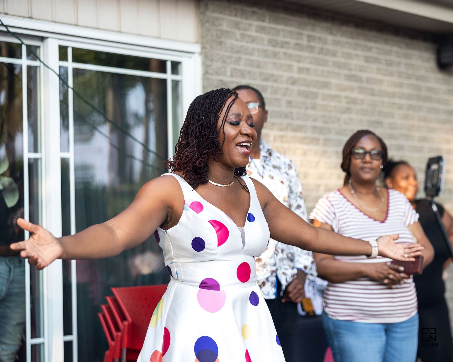 Woman in polka dot dress dancing and celebrating outdoors by brick building.