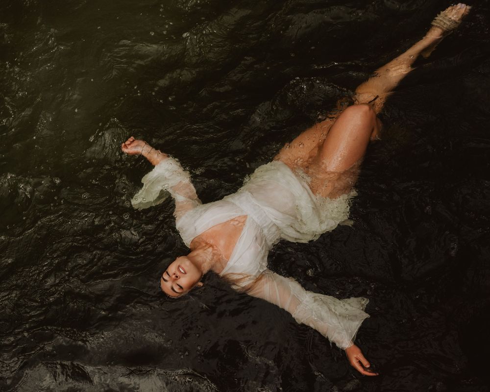 An ethereal figure in a flowing white dress floats gracefully against a dark background in a dreamy artistic photograph.