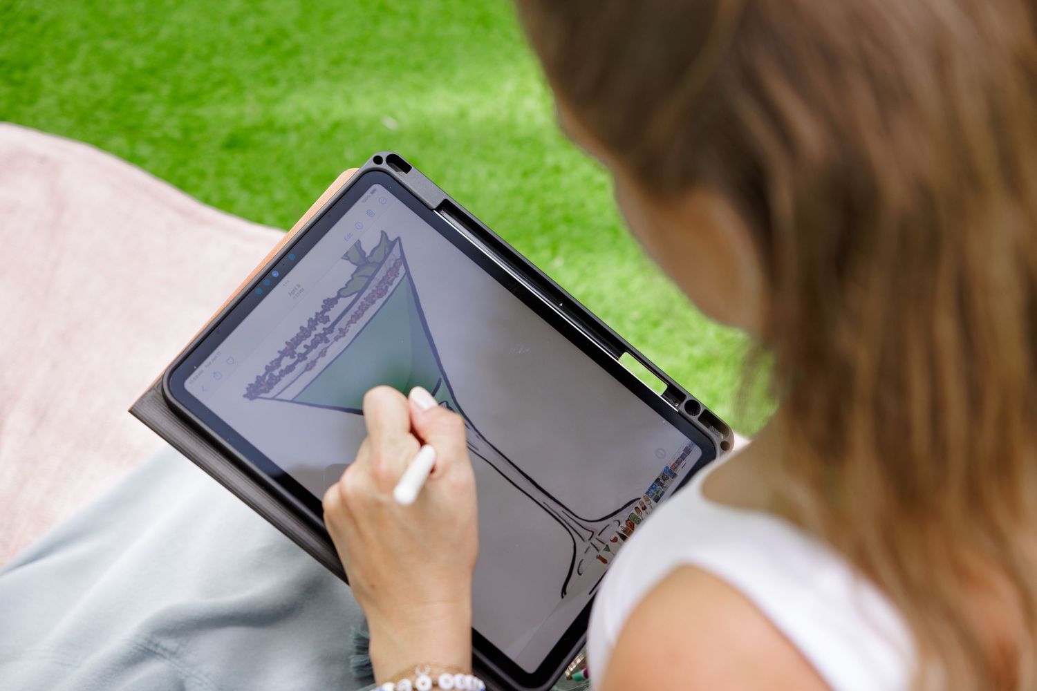 Person using digital tablet outdoors on bright green lawn.