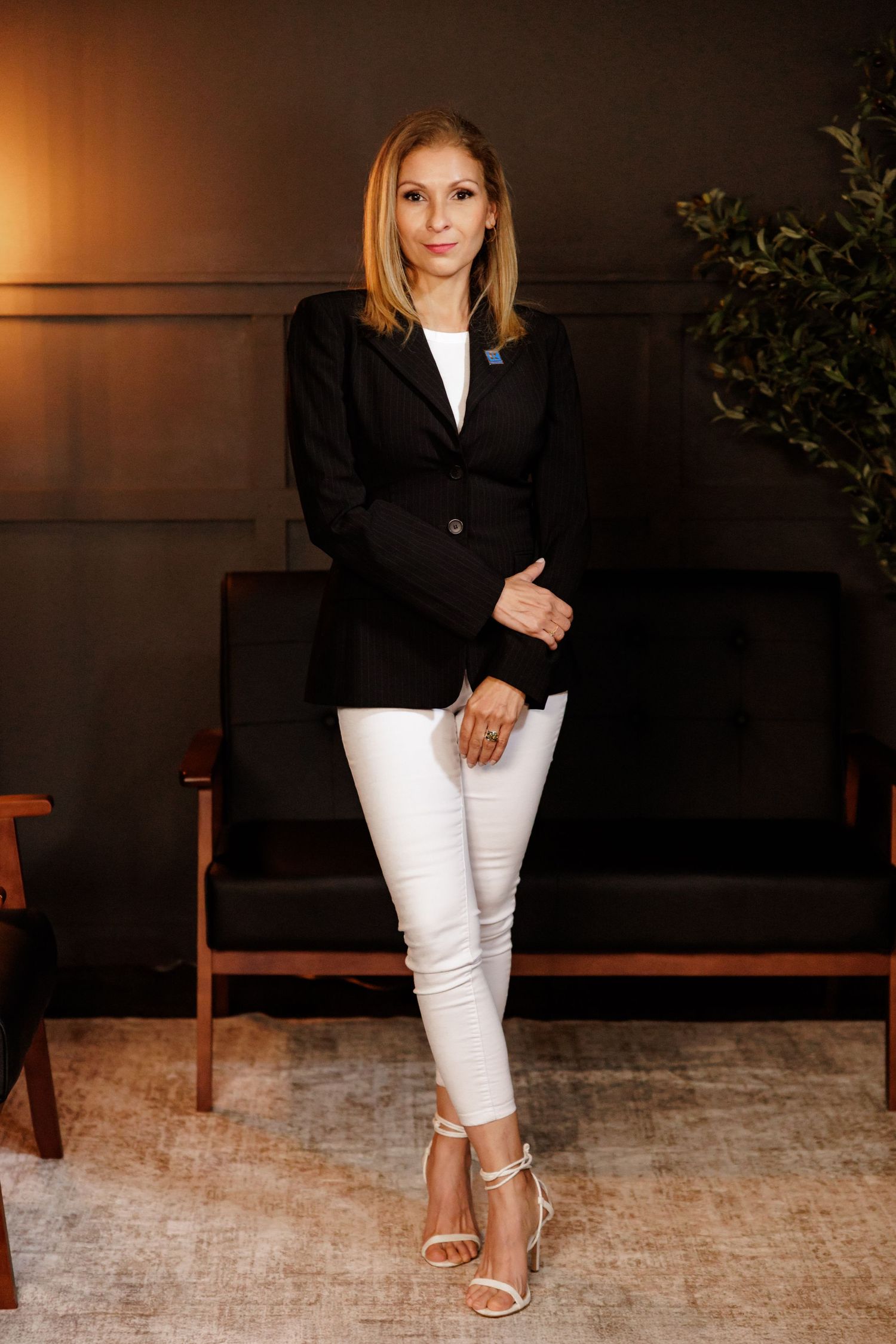 Professional fashion photoshoot featuring black blazer and white pants against dark backdrop.