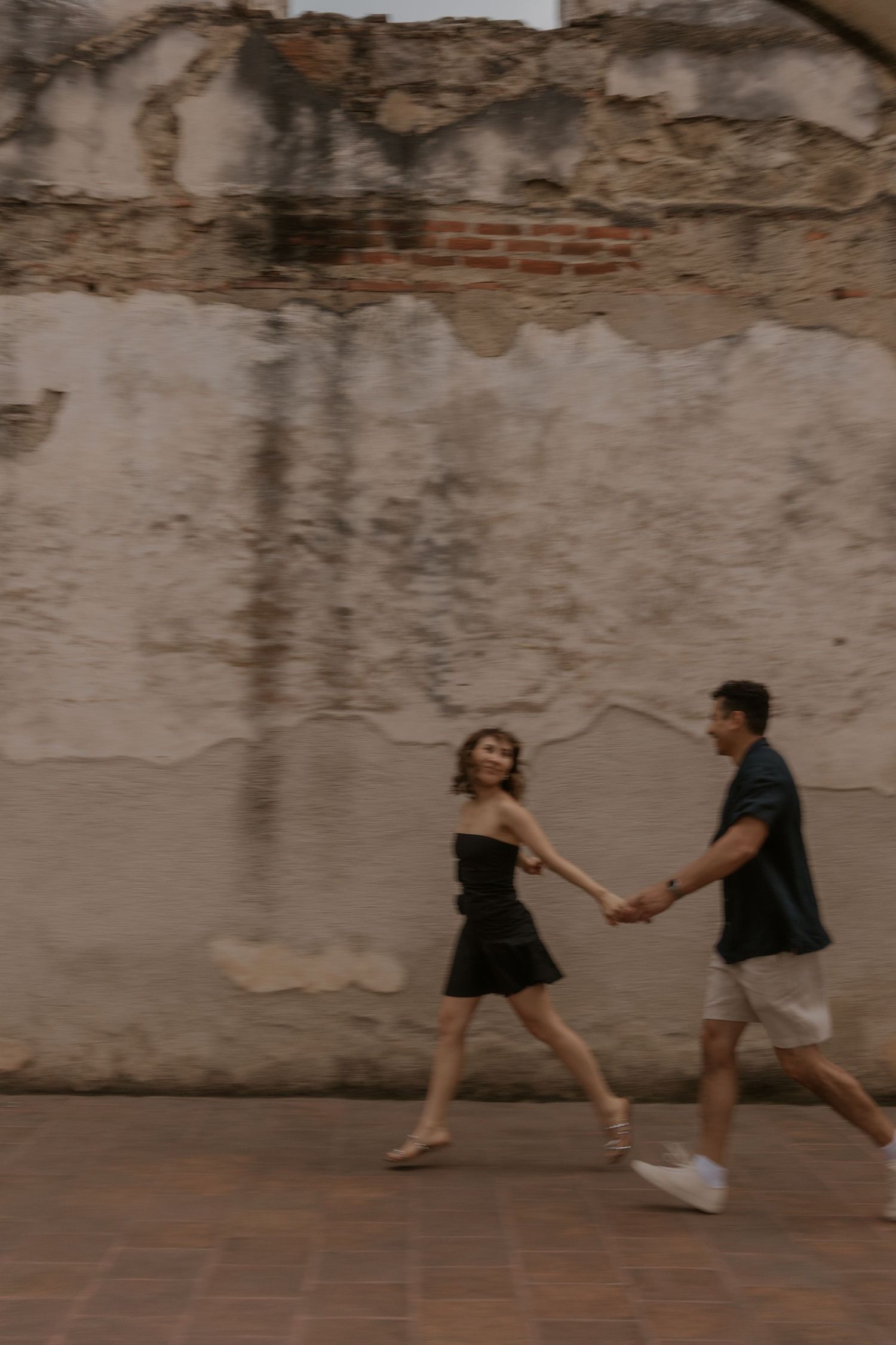 A couple dances playfully on a cobblestone street in front of colonial buildings.