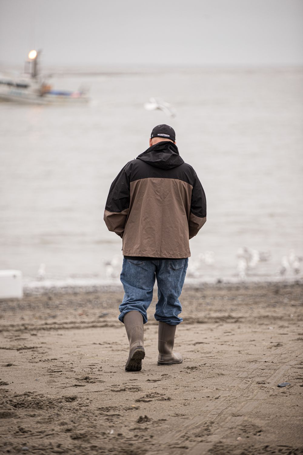 Person in brown jacket and jeans walks along a misty beach.