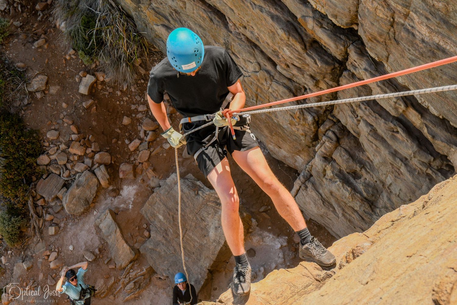 Rock climber in safety gear rappelling down a steep cliff face with ropes. (Optical Josh)