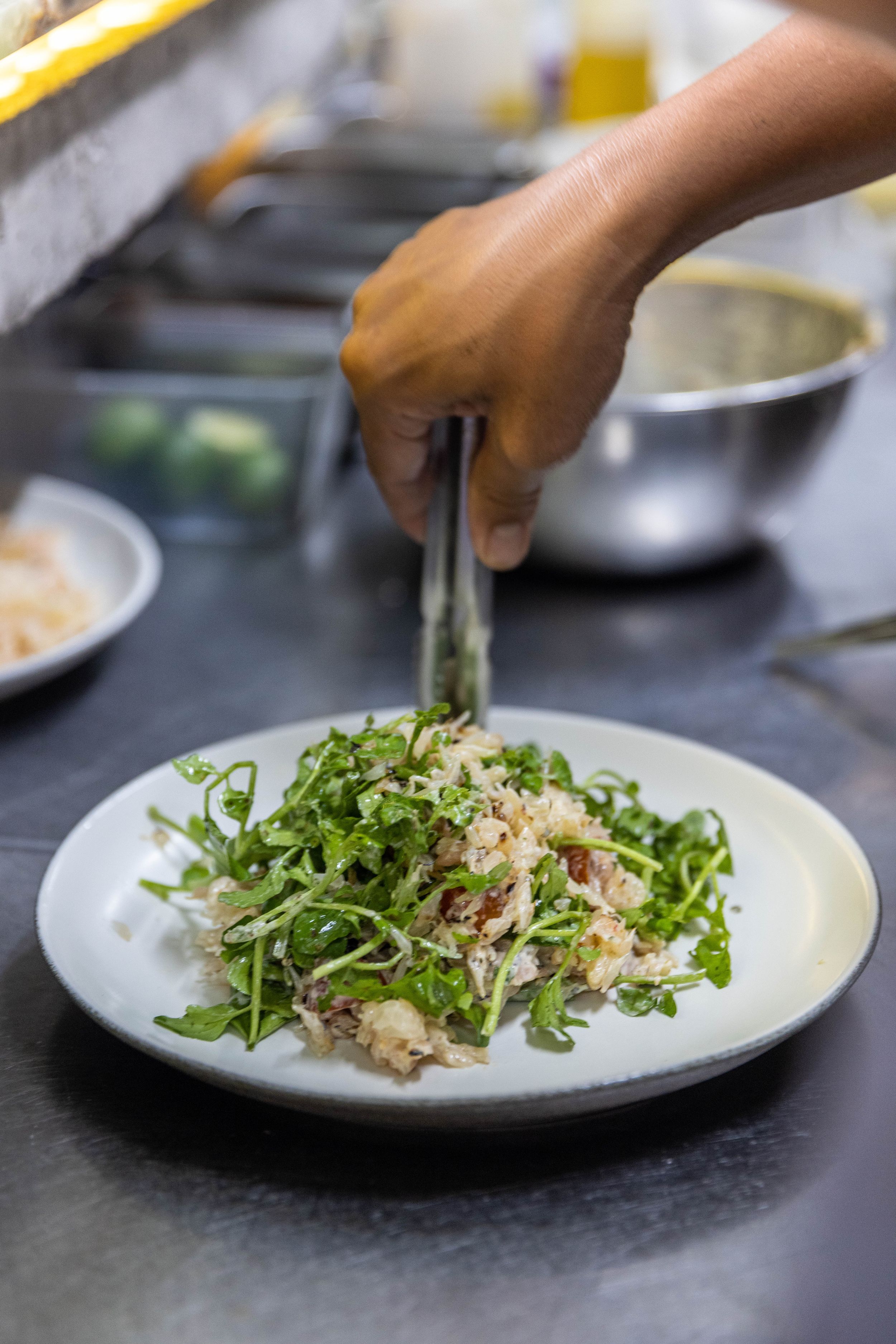Chef plating a fresh arugula salad in restaurant kitchen.