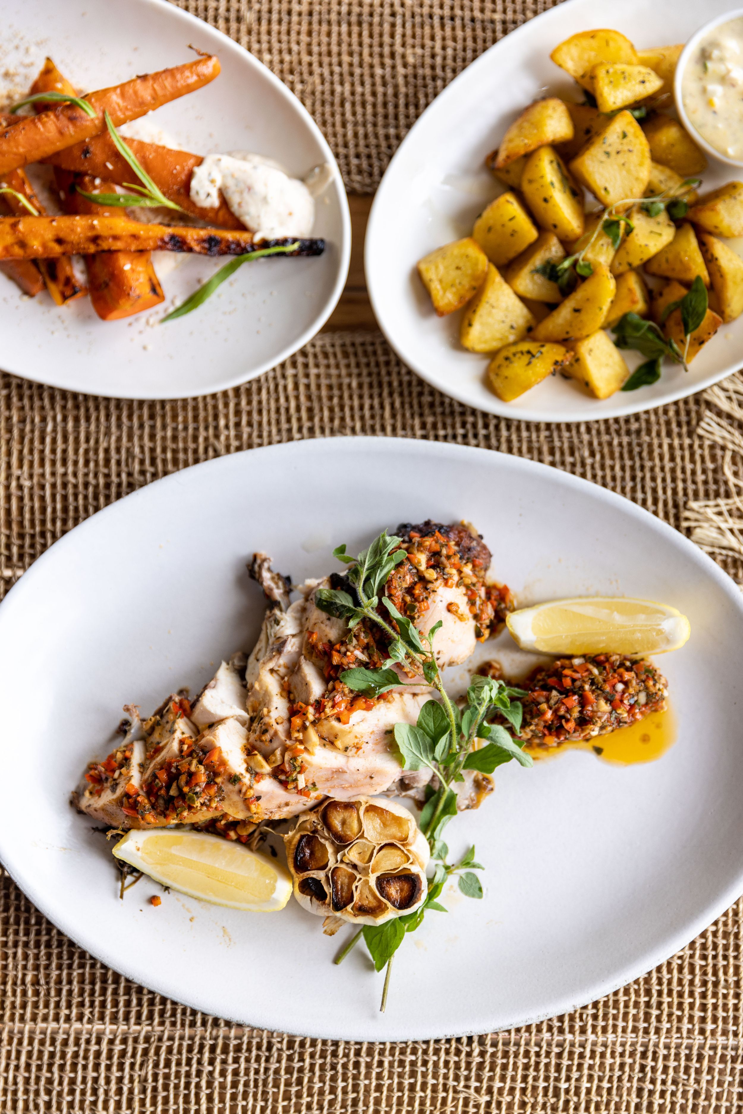 Grilled fish with roasted carrots and crispy potatoes served on white plates.