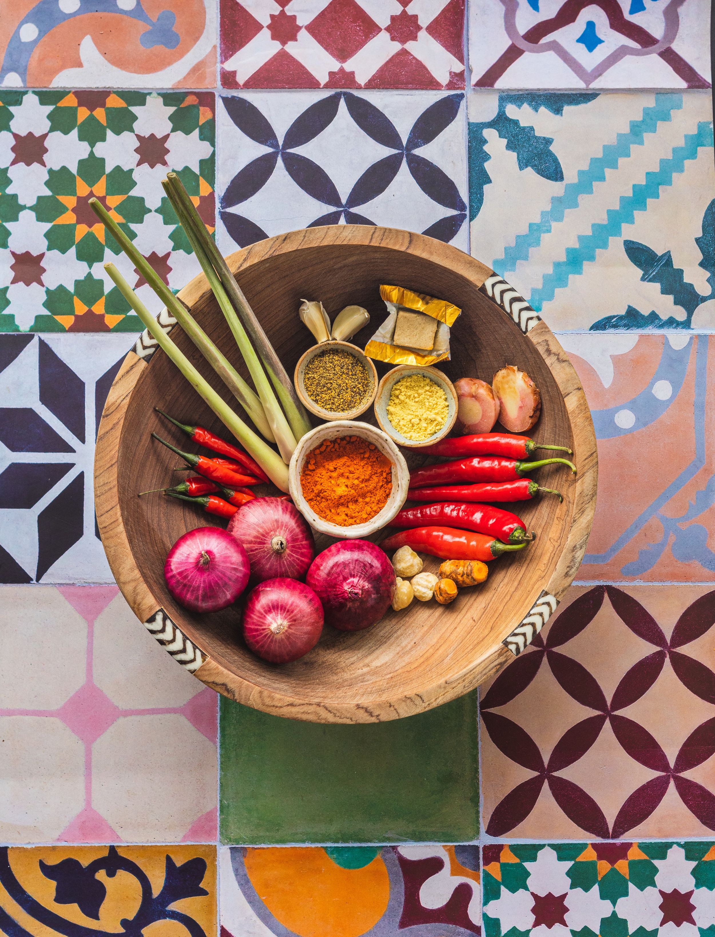 Colorful spices and fresh ingredients in wooden bowl on decorative tile background.