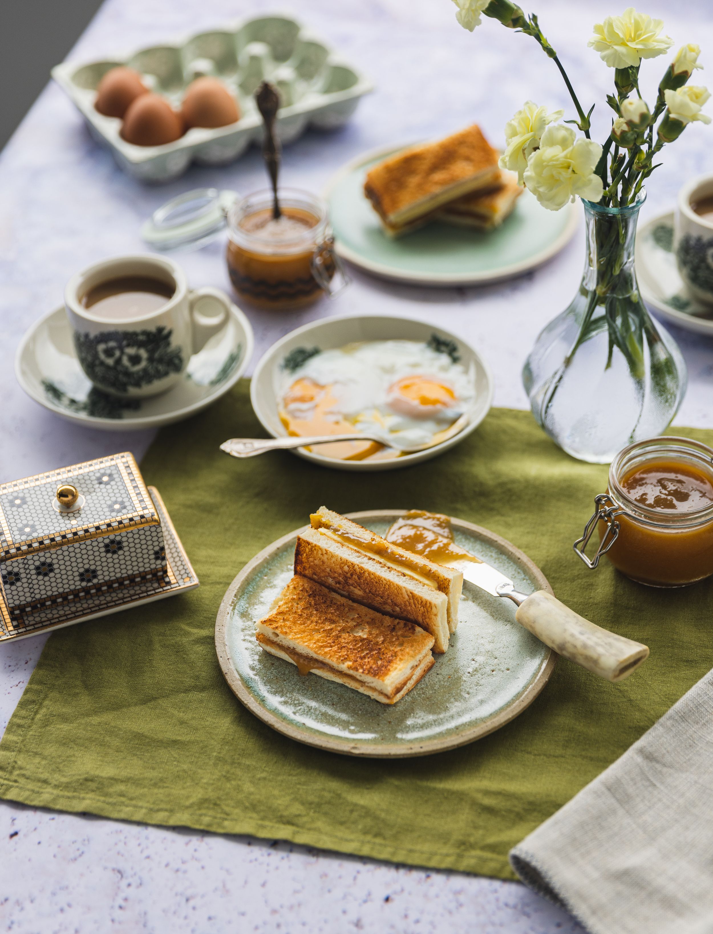 Breakfast table setting with toast, eggs, coffee and fresh flowers on green placemat.