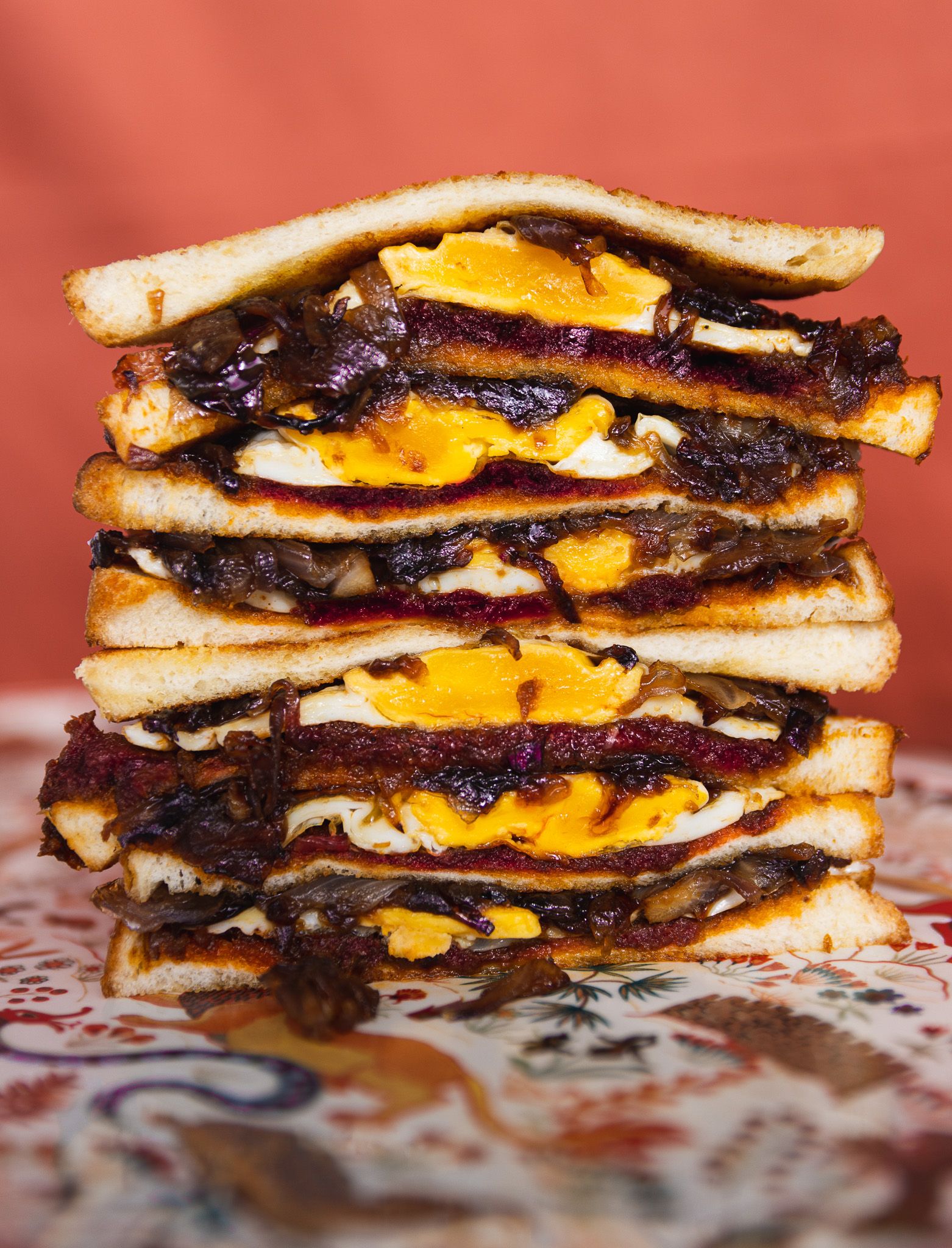 Towering stack of grilled cheese sandwiches with melted cheddar and caramelized onions on toasted bread.