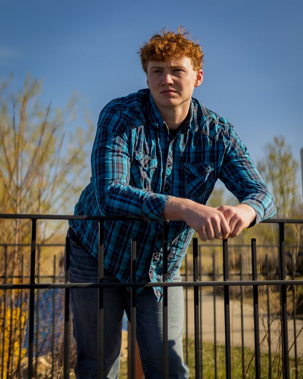 High school senior, flannel shirt and jeans posing for senior pictures in the Boise Idaho Treasure Valley area with trees.