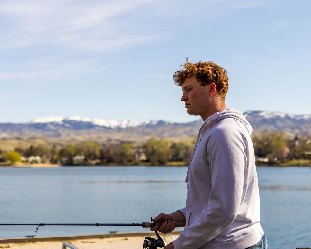 High School senior in light colored sweatshirt fishing at a lake in Boise Idaho Treasure Valley area