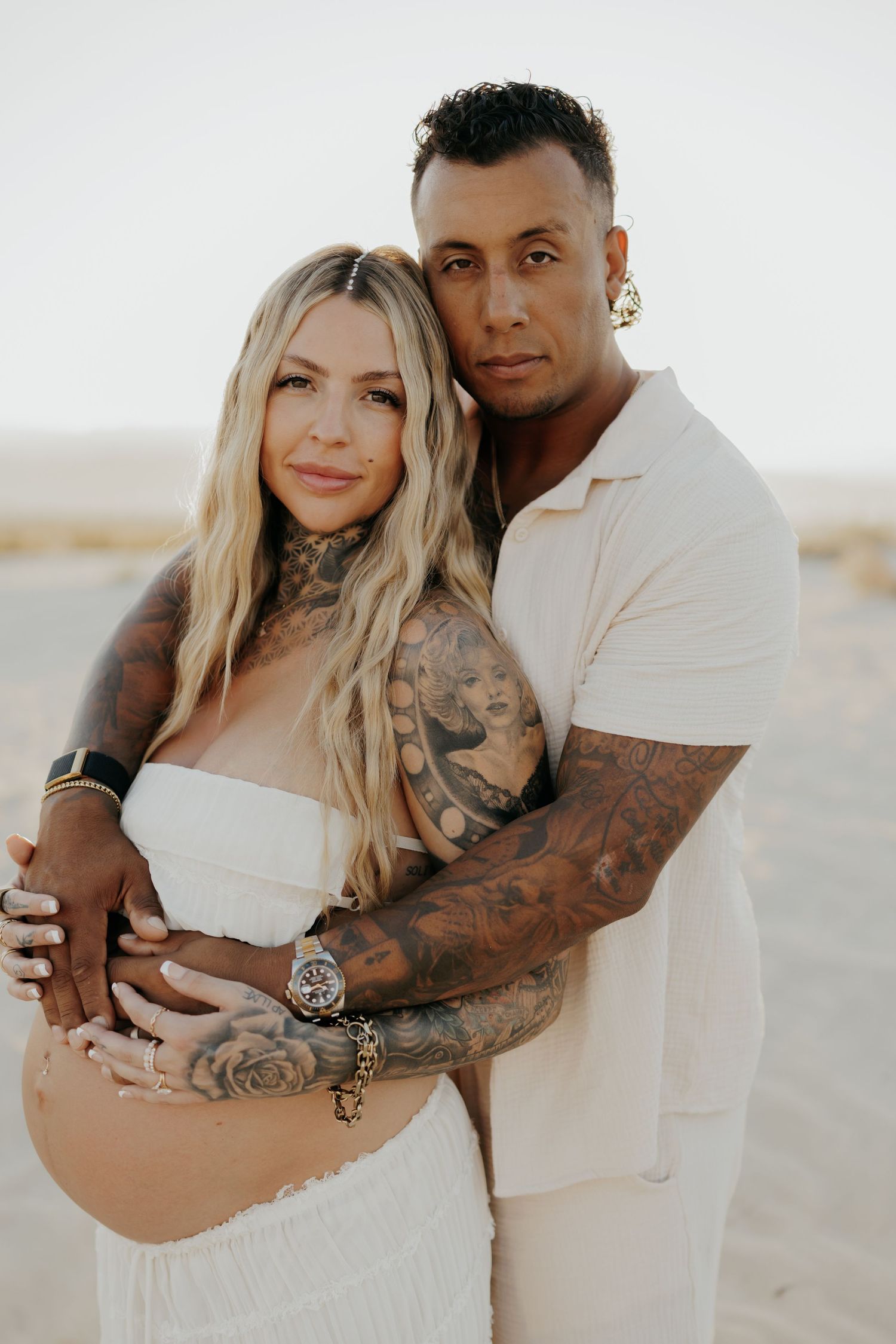 Desert maternity portrait of couple in matching white outfits during golden hour.