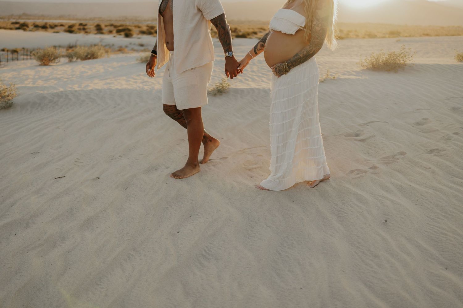 Close-up of feet and flowing white clothing on sandy desert terrain.