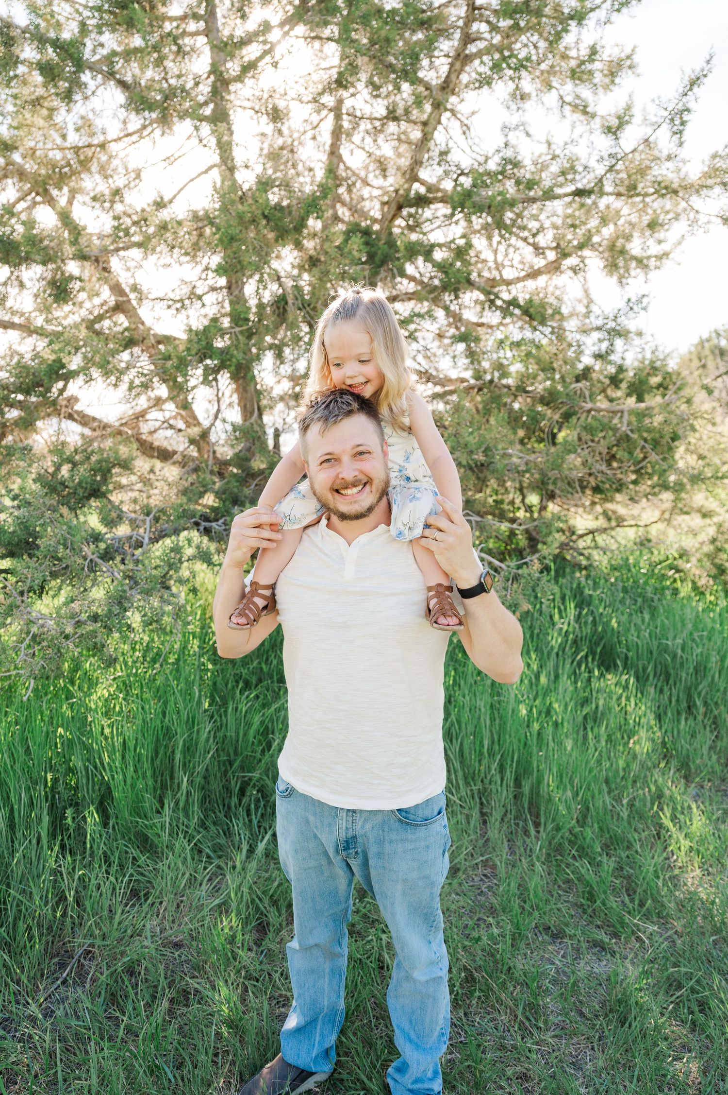 A joyful moment outdoors with someone carrying a child on their shoulders among spring foliage.