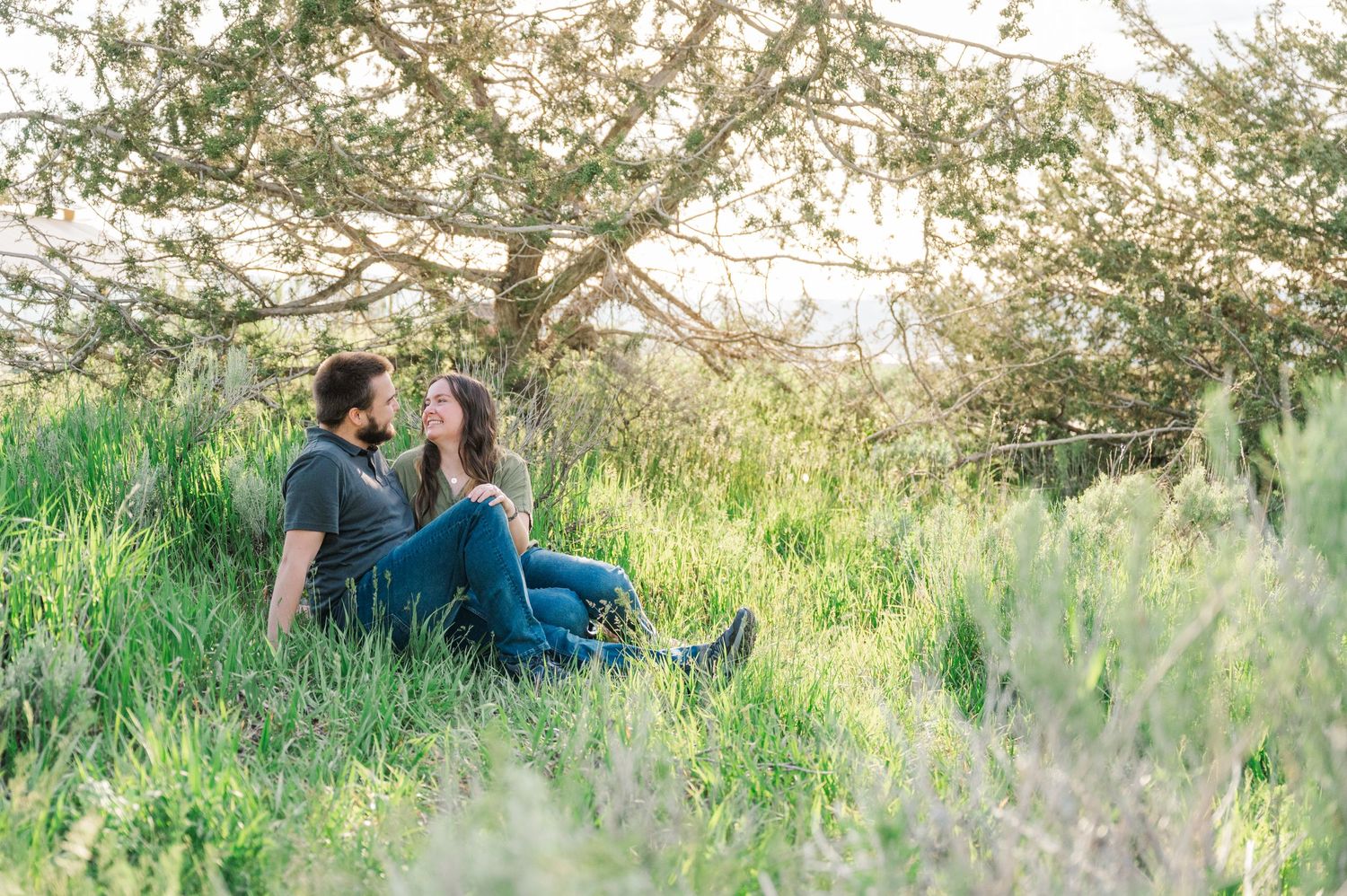 A couple sits together on a grassy hillside during golden hour.