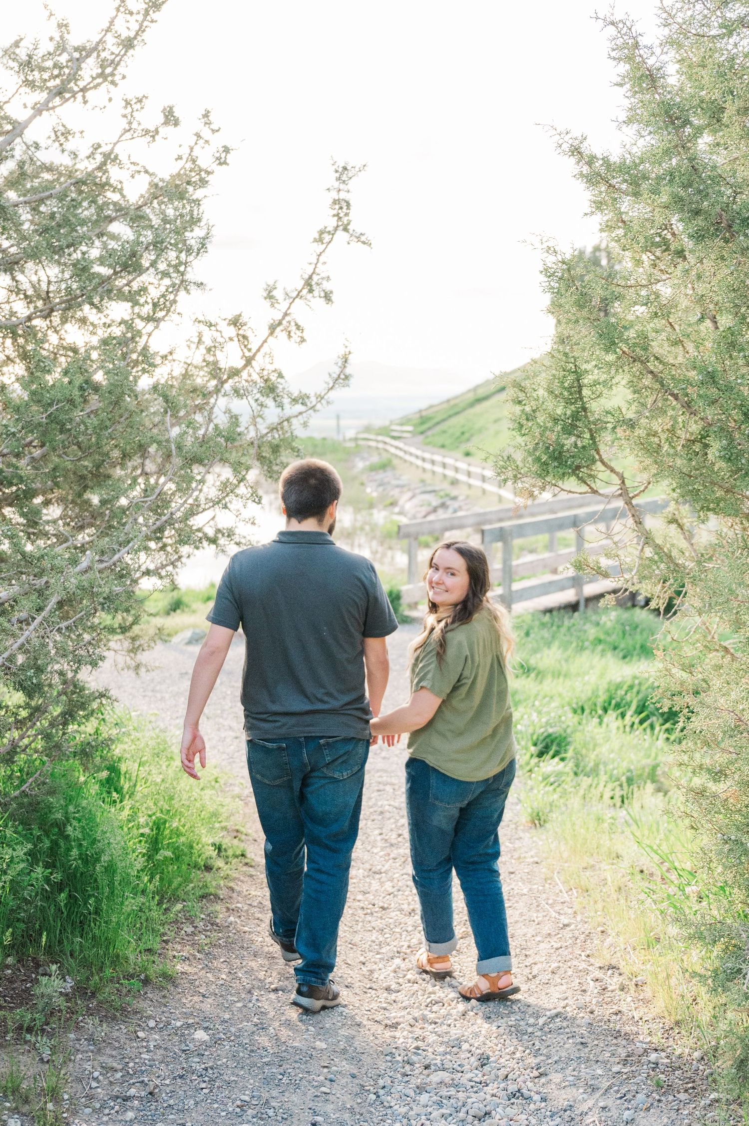 A couple walking on a scenic mountain trail, looking back at the camera.