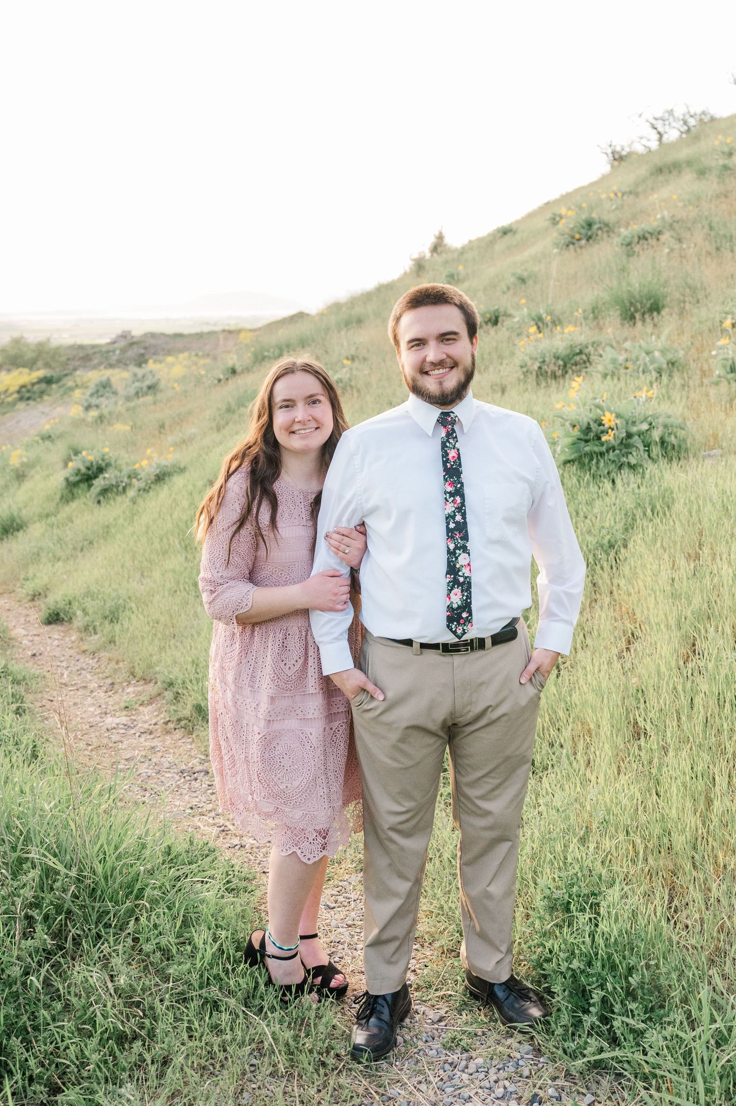 A couple shares a tender moment on a hillside trail during golden hour.