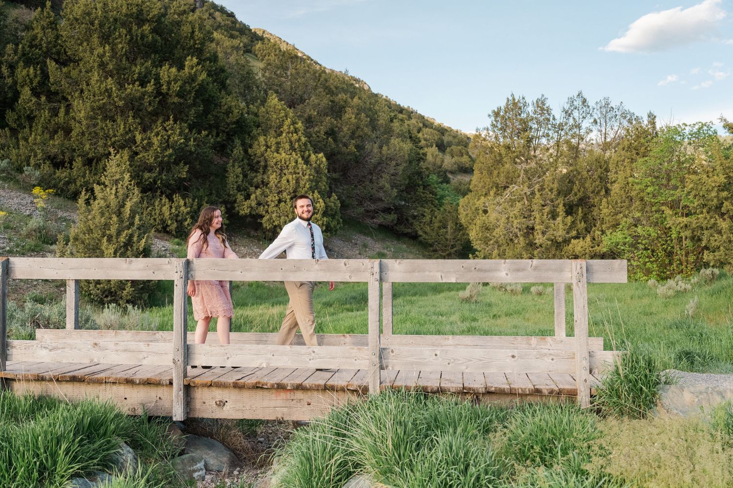 A couple shares a playful moment on a wooden footbridge surrounded by nature.