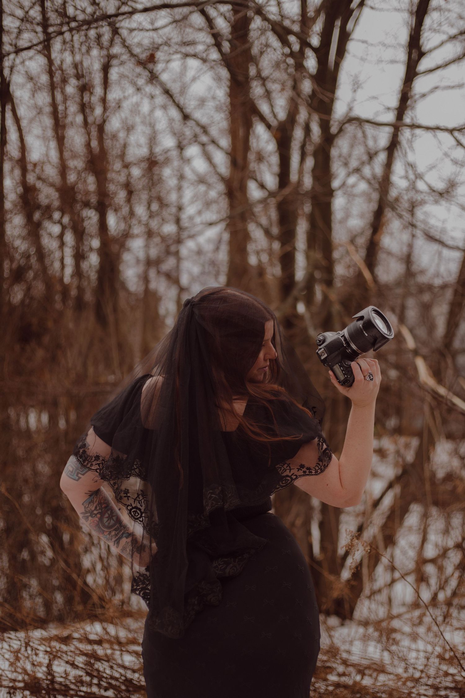 Melissa wandering through the woods with her camera and a black veil covering her head.