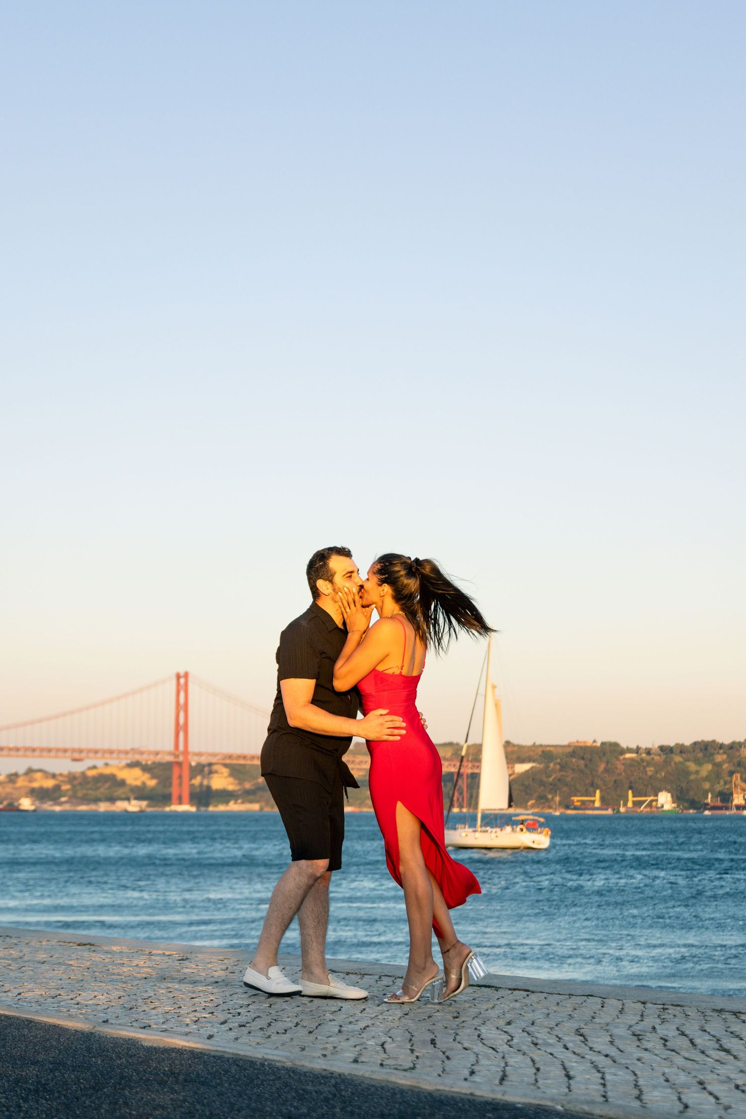 A romantic couple shares a kiss at sunset with the iconic Golden Gate Bridge visible in the background.