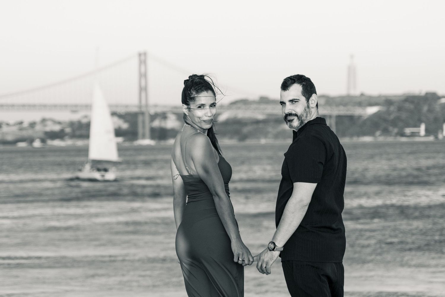 A couple in casual attire walks and talks together on a grassy field in black and white.