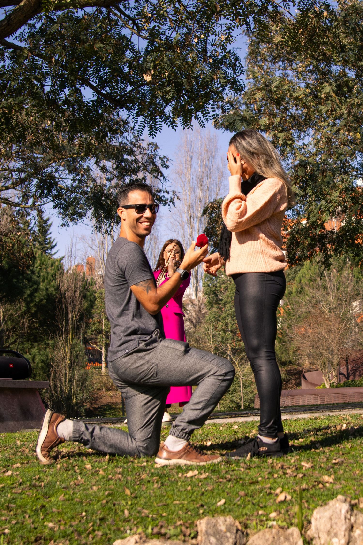 A surprise proposal sequence captured outdoors on a grassy lawn during autumn.