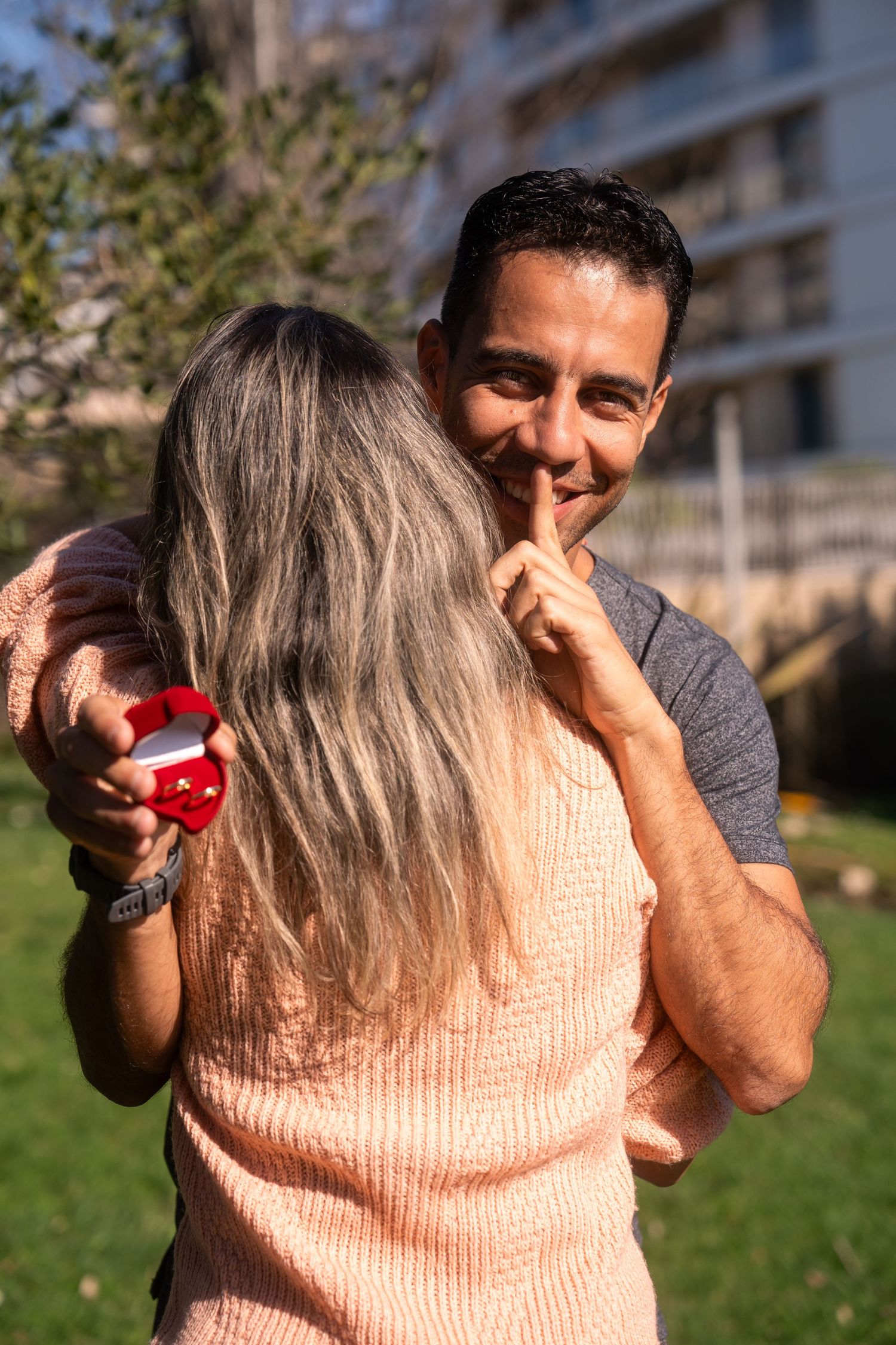A heartwarming proposal scene with a red ring box in a park setting.