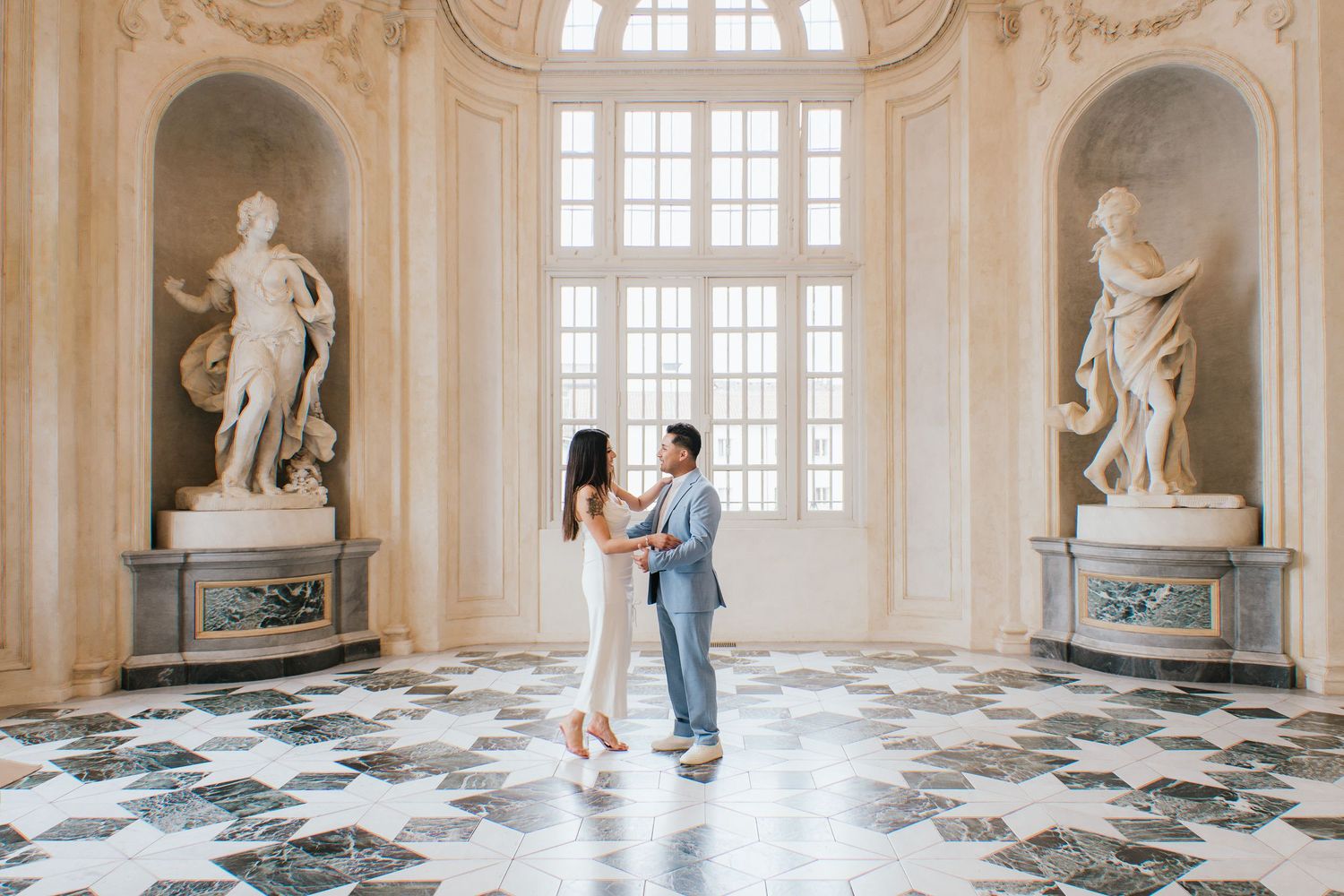 A couple dances in an elegant baroque palace hall with marble floors and classical statues in ornate alcoves.