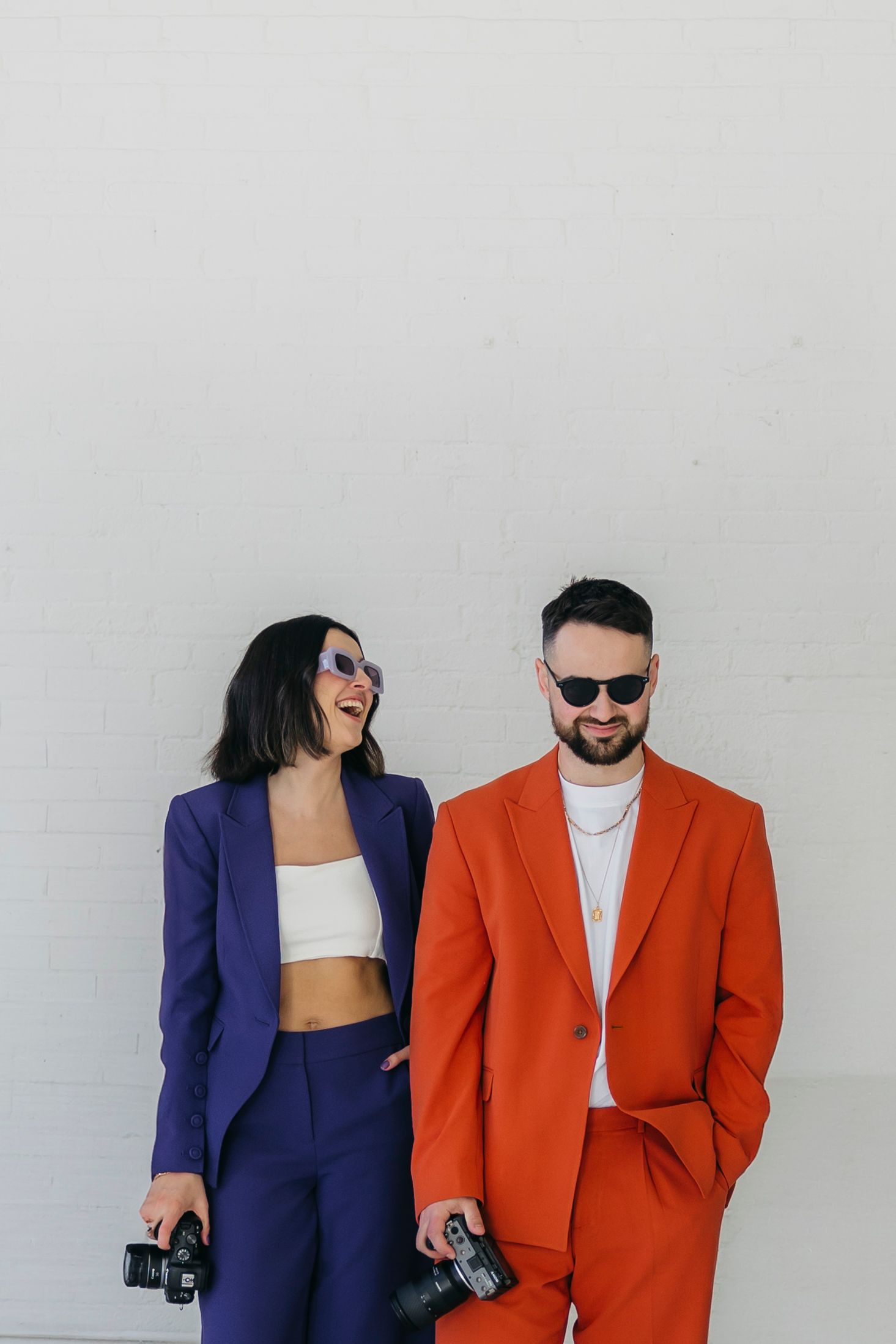 Stylish duo in contrasting blue and orange blazers posing against white wall.