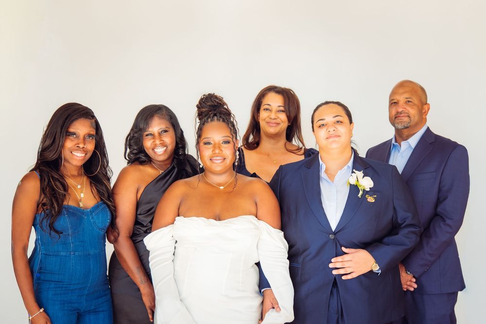 Wedding party poses together in formal attire against a white background.