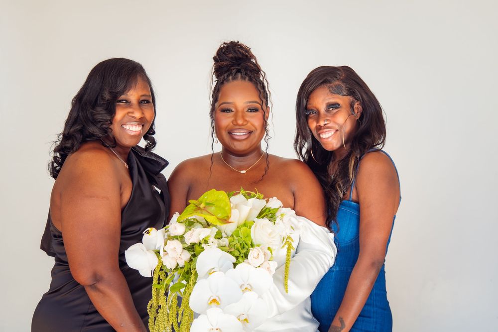 Bridesmaids in blue dresses gather around white floral bouquets for a group photo.
