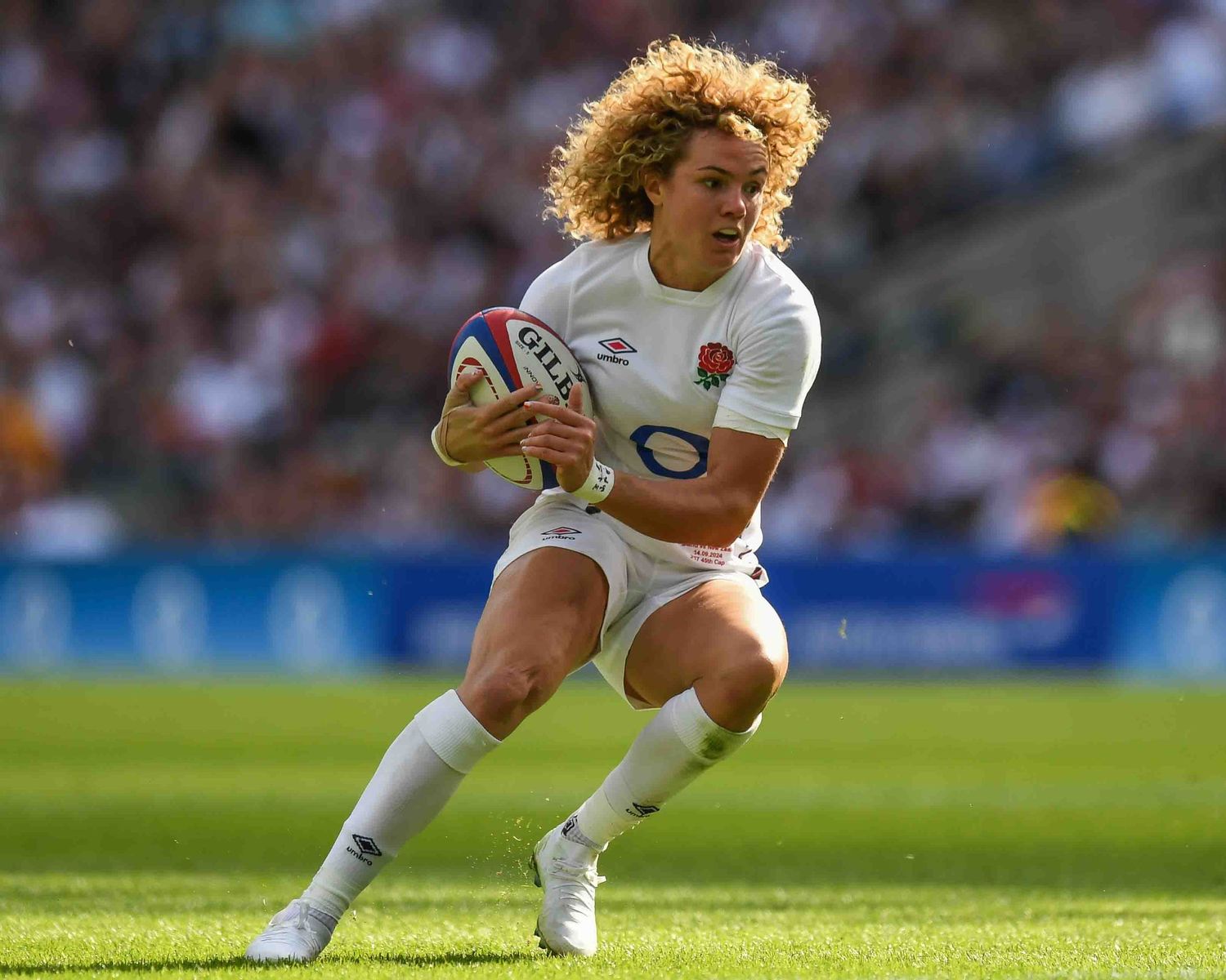 Rugby player carrying ball during match in white uniform.