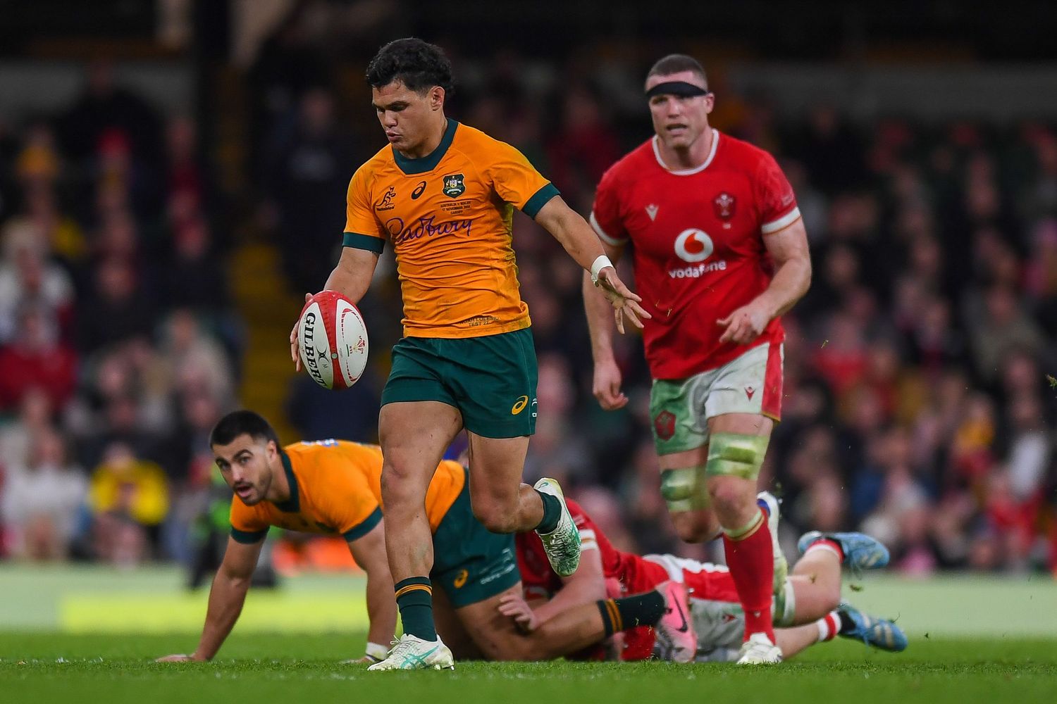 Rugby player in orange jersey carries ball while evading tackles.