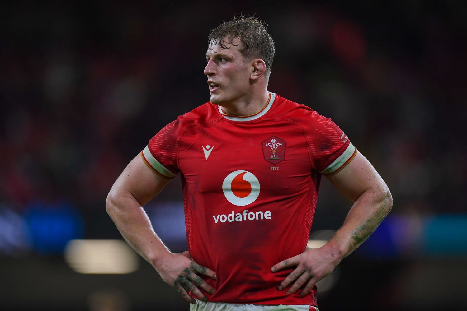 Rugby player in red Vodafone jersey stands during match with hands on hips.